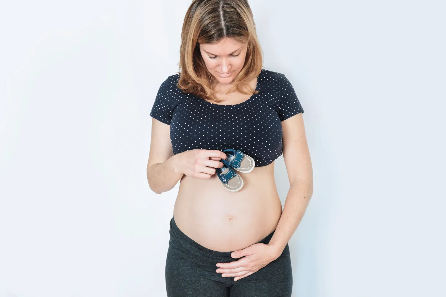 Mujer embarazada sosteniendo zapatos de bebé mientras toca su vientre, representando los cambios físicos y emocionales del primer trimestre del embarazo.